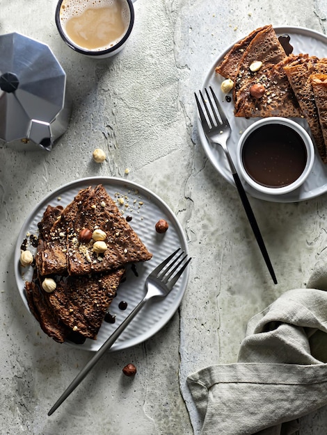 Photo two plates of chocolate pancakes with nuts and chocolate sauce on a textured background top view