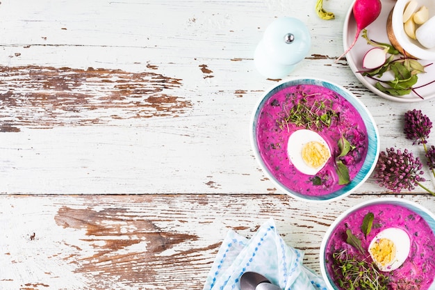 Two plates of cold summer beetroot, cucumber and egg soup on a wooden table. Top view. Copy space.