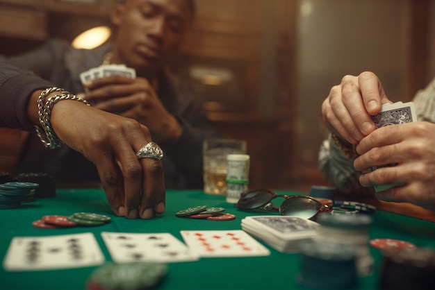 Two poker players place bets on gaming table with green cloth in casino. Games of chance addiction, risk, gambling house. Men leisures with whiskey and cigars