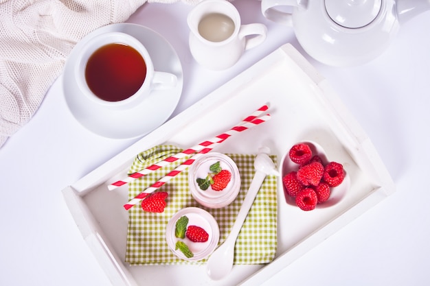 Two portions natural homemade yogurt in a glass jar with fresh raspberry on the white tray. Breakfast concept. Top view.