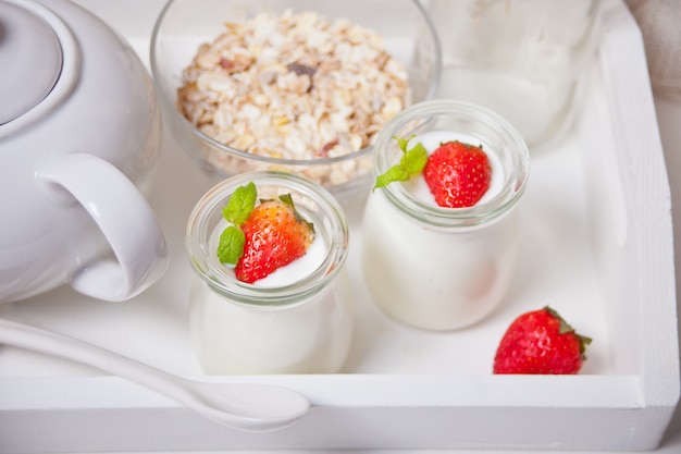 Две порции натурального домашнего йогурта в стеклянной банке со свежей клубникой и миской мюсли