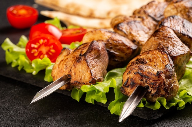 Two portions of shish kebab on a stone plate with salad, sliced pita bread, cherry tomatoes