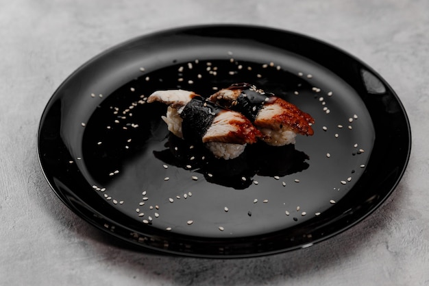 Photo two portions of sushi with shrimp and eel on a black plate on a gray background