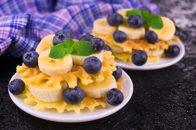 Две порции вафель с ягодами и бананом на белой тарелке Вкусный завтрак крупным планом