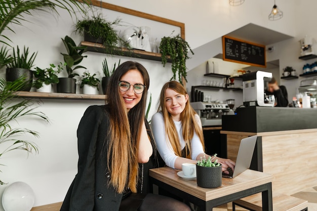 Two positive girlfriends in formal wear relaxing in a coffee shop