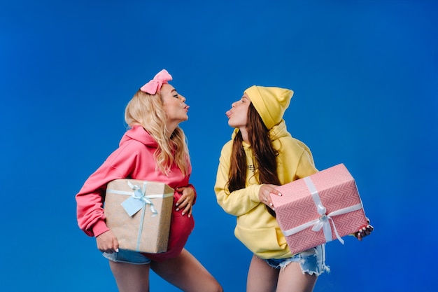 Two pregnant girls with gifts in their hands on a blue isolated background