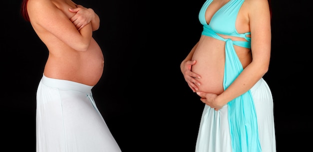 Photo two pregnant women showing their beautiful bellies isolated on a black background