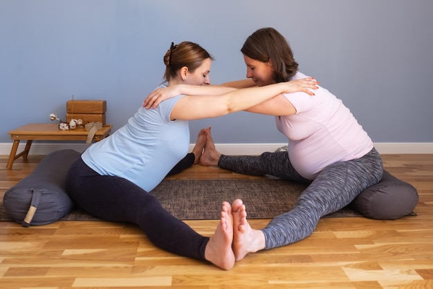 Two pregnant women working out idoing Seated straddle posture Upavishtha Konasana