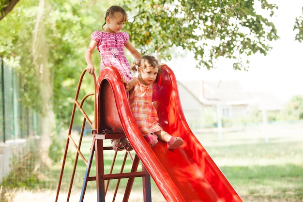 Due bambine in età prescolare sullo scivolo al parco giochi