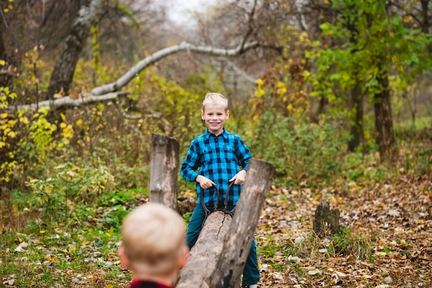 Two preteen brothers, friends found handmade swing from wood and ropes during family weekend in autumn forest, childhood adventures
