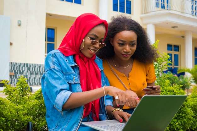 Two pretty african ladies pointing at what they saw on the\
laptop.