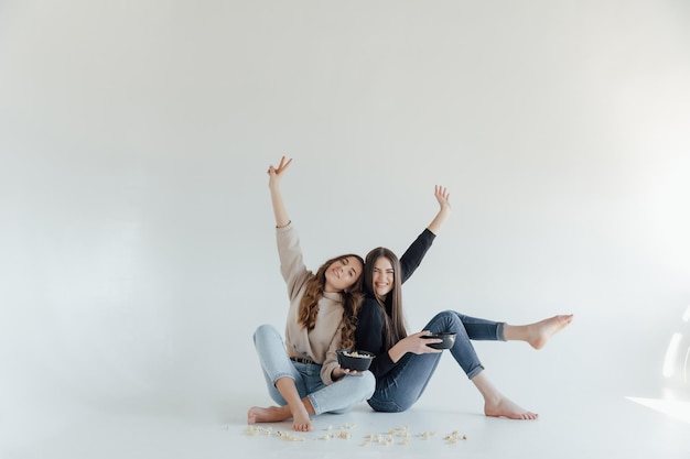 Two pretty cheerful young girls friends standing isolated over white background, eating popcorn