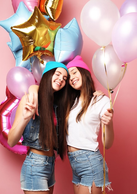 two pretty emotional girls hold balloons and posing against pin