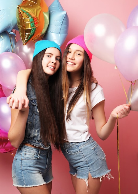 two pretty emotional girls hold balloons and posing against pink wall