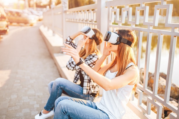 Two pretty girls enjoy virtual reality glasses outdoor