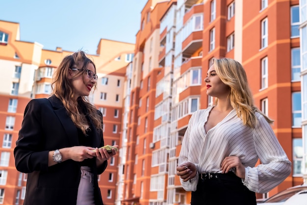 Two pretty real estate agents  while standing near a house for sale outdoor