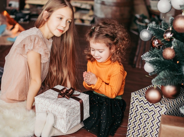 Two pretty sisters with presents sitting on the floor on Christmas eve. holiday concept