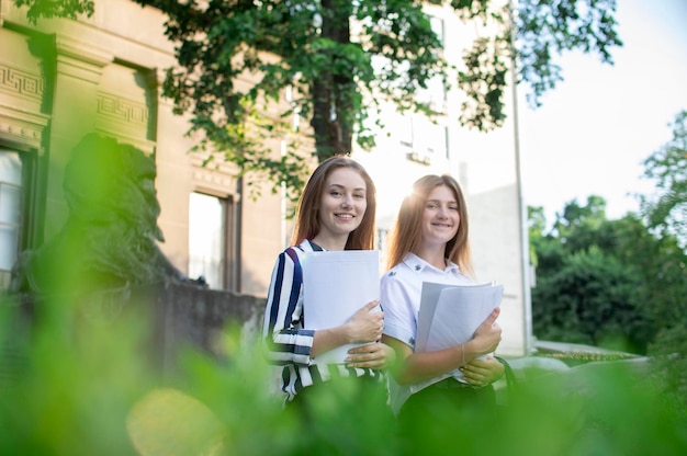 Two pretty students are standing near the university holding papers