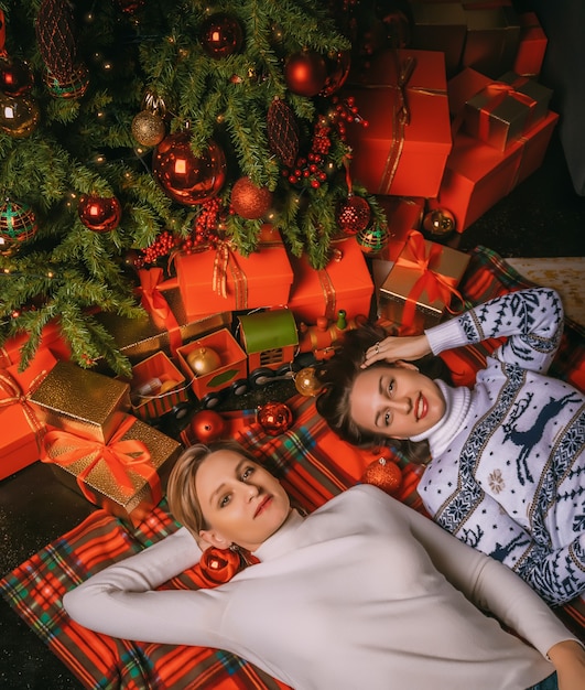 두 예쁜 여자가 선물 상자와 함께 실내 축제 전나무 아래 닫습니다. 크리스마스 photo