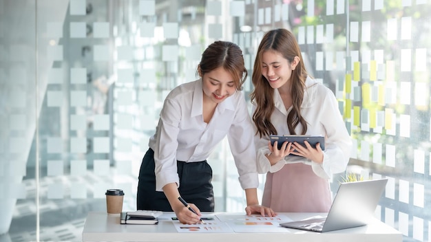 Due piuttosto giovani asiatici imprenditrice in piedi lavorando insieme a discutere di relazione finanziaria del progetto concetto di collaborazione aziendale aziendale