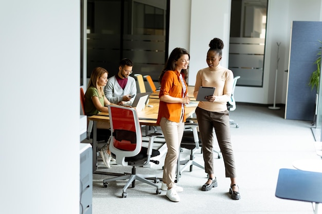 Two pretty young business women with digital tablet in the modern office in front of their team