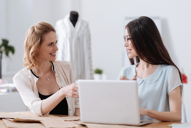 Two pretty young female colleagues looking at each other, smiling and discussing their work plans