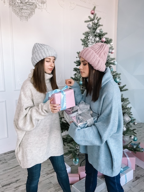 Two pretty young girls wearing sweaters unpaking gifts near the Christmas tree