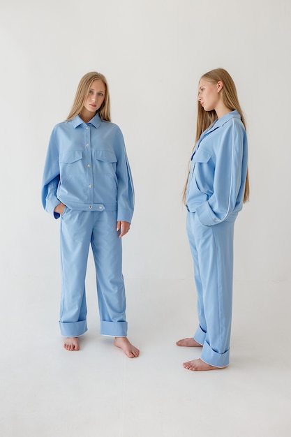 Two pretty young twin sisters with long blond hair posing on white background in oversize clothes. fashion photoshoot