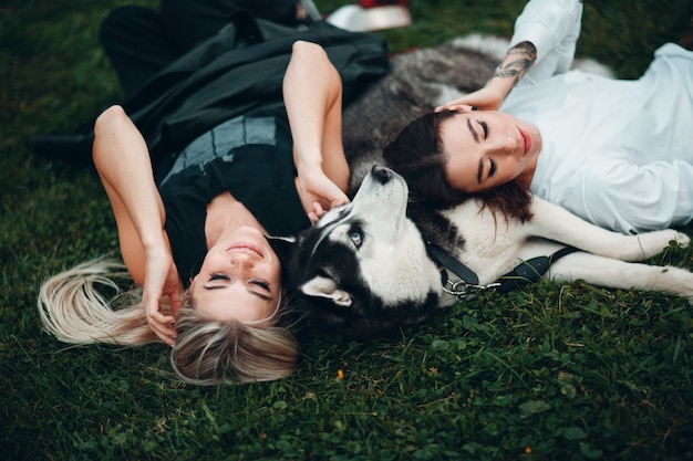 Two pretty young woman laying with husky dog on the grass