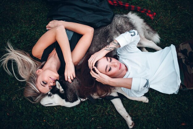 Two pretty young woman laying with husky dog on the grass