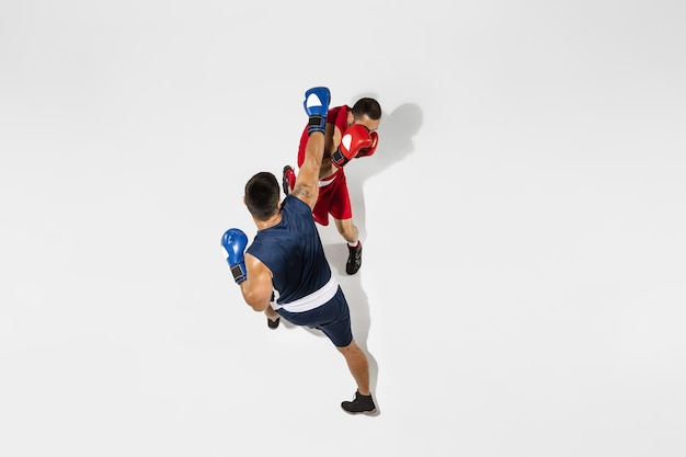 Two professional boxers boxing isolated on white studio background, action, top view. Couple of fit muscular caucasian athletes fighting. Sport, competition, excitement and human emotions concept.