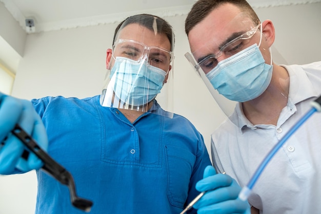 Two professional confident dentists posing near a dental chair in a clinic