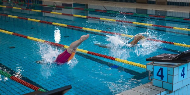 Two professional female swimmers taking track start position on the platform gracefully jumping and