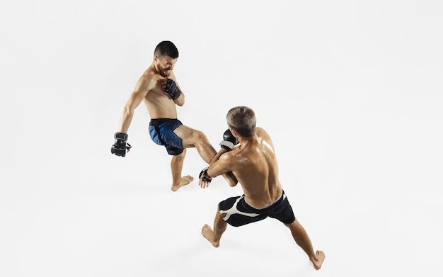 Two professional MMA fighters boxing isolated on white studio background. Top view of couple of muscular athletes. Sport, healthy lifestyle, competition, dynamic and motion, action concept. Copyspace.