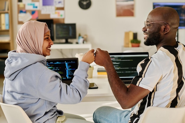 Two programmers giving highfive to each other while sitting at their workplace with computers