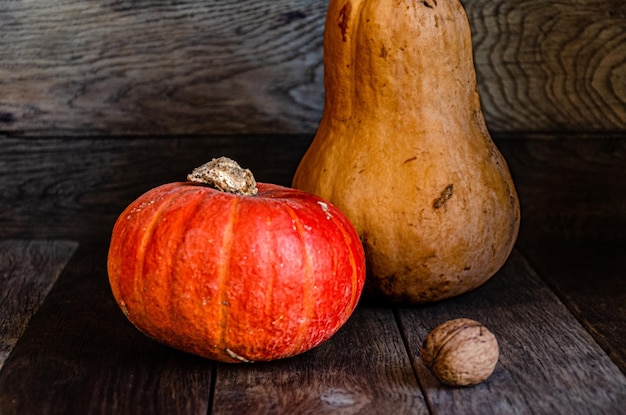 Two pumpkins of different shapes and colors on a wooden background.