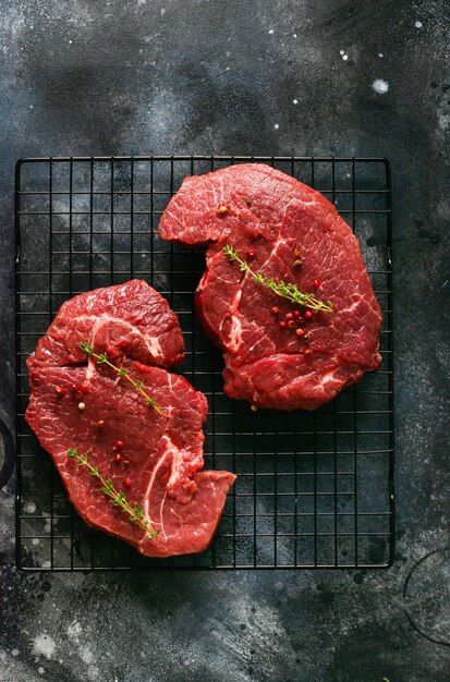 Two Raw beef steak with spices, onions and chili on dark slate or concrete table. Top view