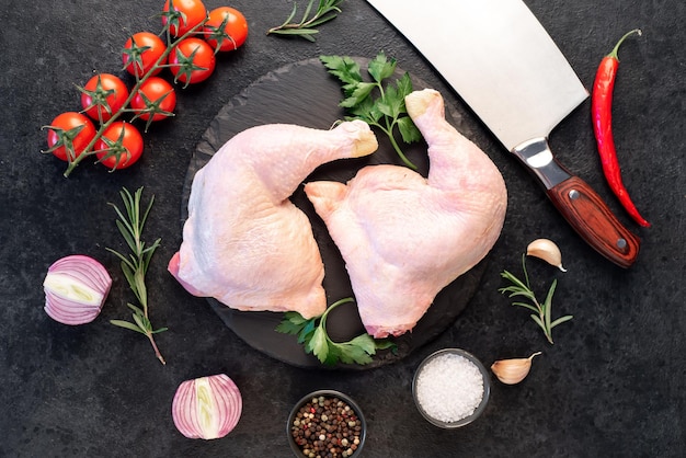 two raw chicken legs with spices and herbs on a stone background
