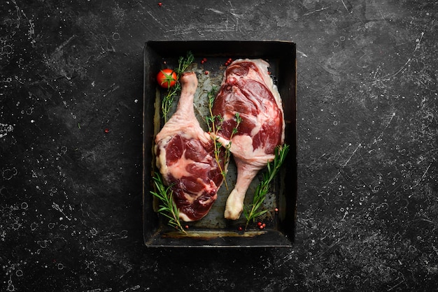 Two raw duck thighs with rosemary and spices On black stone background Top view