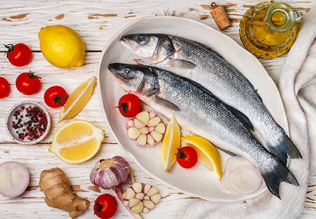 Two raw fresh sea bass ready for baking with tomatoes, lemon, red onion, garlic, ginger, parsley and spices