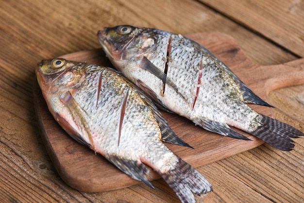 Two raw nile tilapia freshwater fish on wooden wooden board / fresh tilapia fish for cooking food