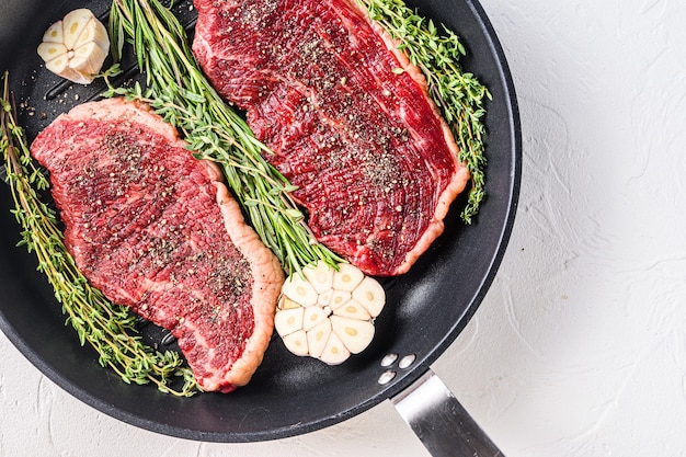 Two raw picanha organic  beef steaks ready for grill on pan with herbs and garlic. Over white textured background, top view, space for text.