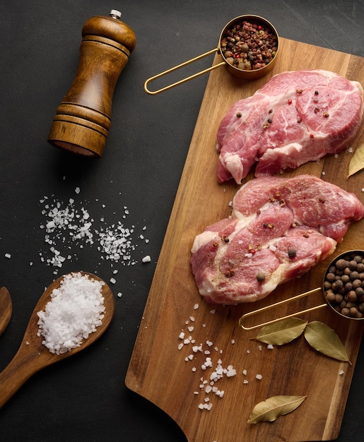 Two raw pork neck steaks on a board and spices for cooking Top view