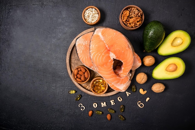 Two raw salmon steaks on a round wooden tray surrounded by ripe avocado, nuts, seeds, omega3 capsules. top view. copy of the space.