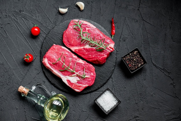 Two raw steaks on a black background with spices and herbs.