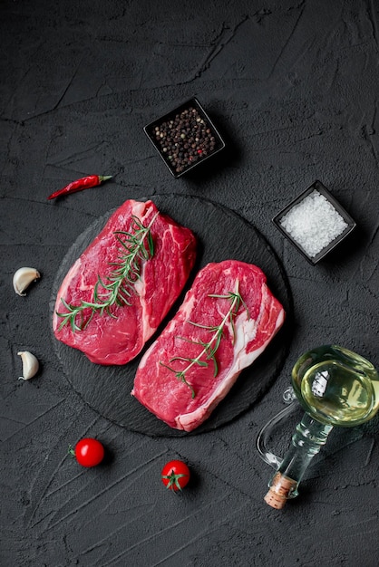 Two raw steaks on a black background with spices and herbs.