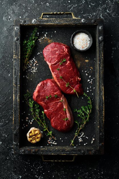 Two Raw striploin steak New York of beef on a board Top view On a black stone background