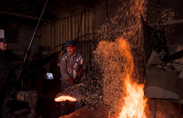 two real brutal traditional blacksmith workers working together with a red hot iron using mechanical hammer at workshop  Portrait of a profession