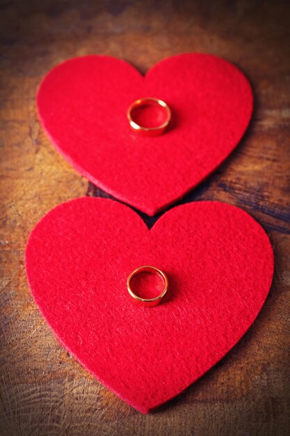 Two red felt hearts and wedding rings on wooden background closeup