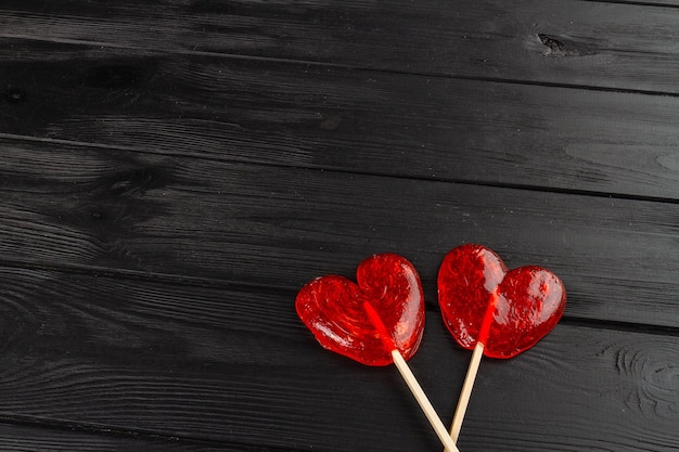 Due lecca-lecca a cuore rosso su scrivania in legno nero amore e concetto di san valentino